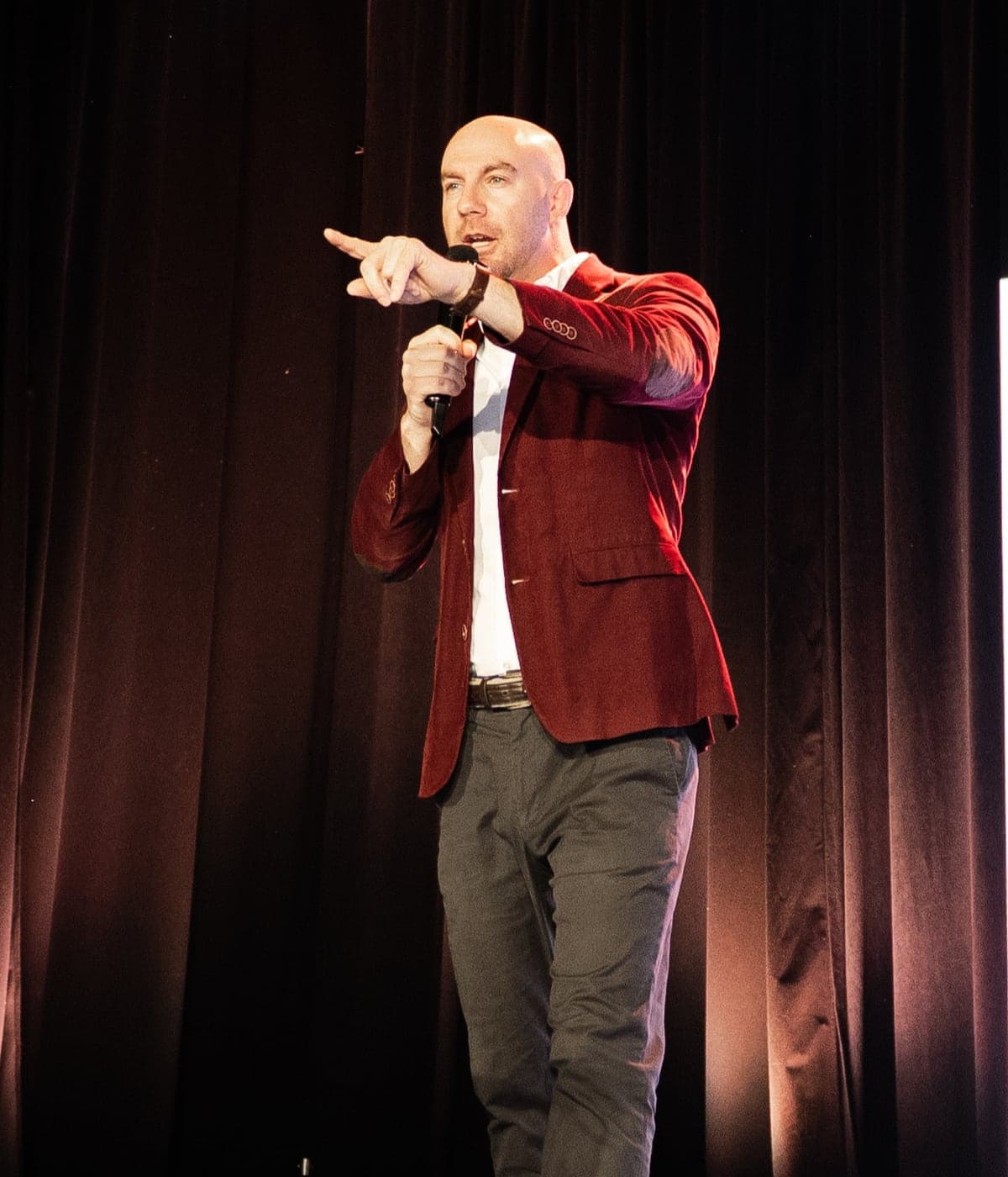 Max in a red blazer on stage, pointing at the audience with a microphone in hand