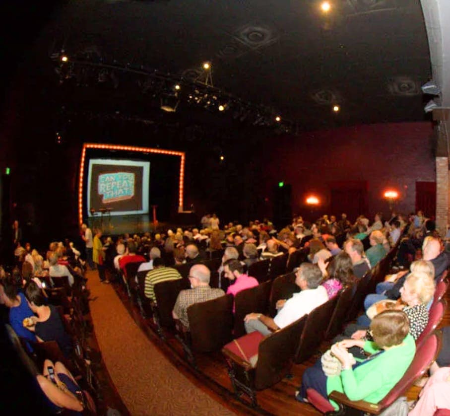 A full theater audience facing the lit game-show stage