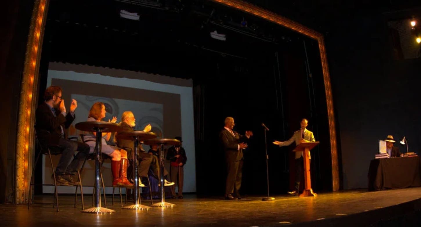 Contestants at their tables while Max hosts from the podium