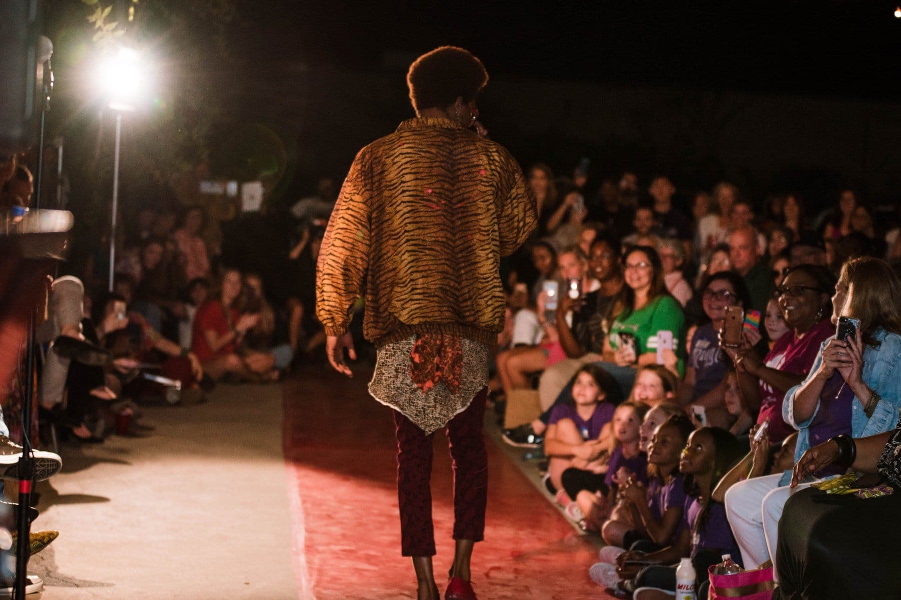 A runway model walking past a packed, cheering audience