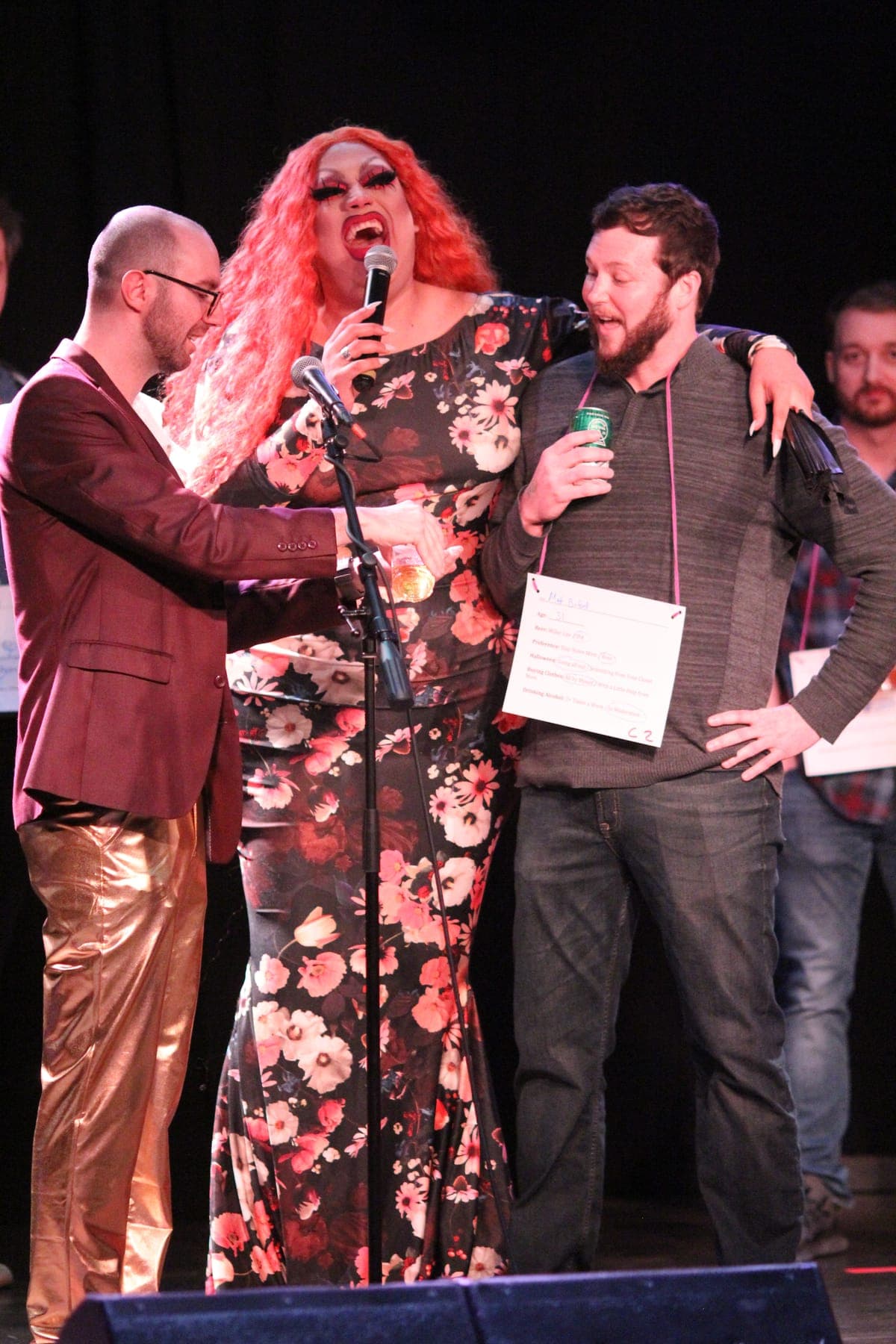 Max and a drag queen co-host laughing on stage with a contestant