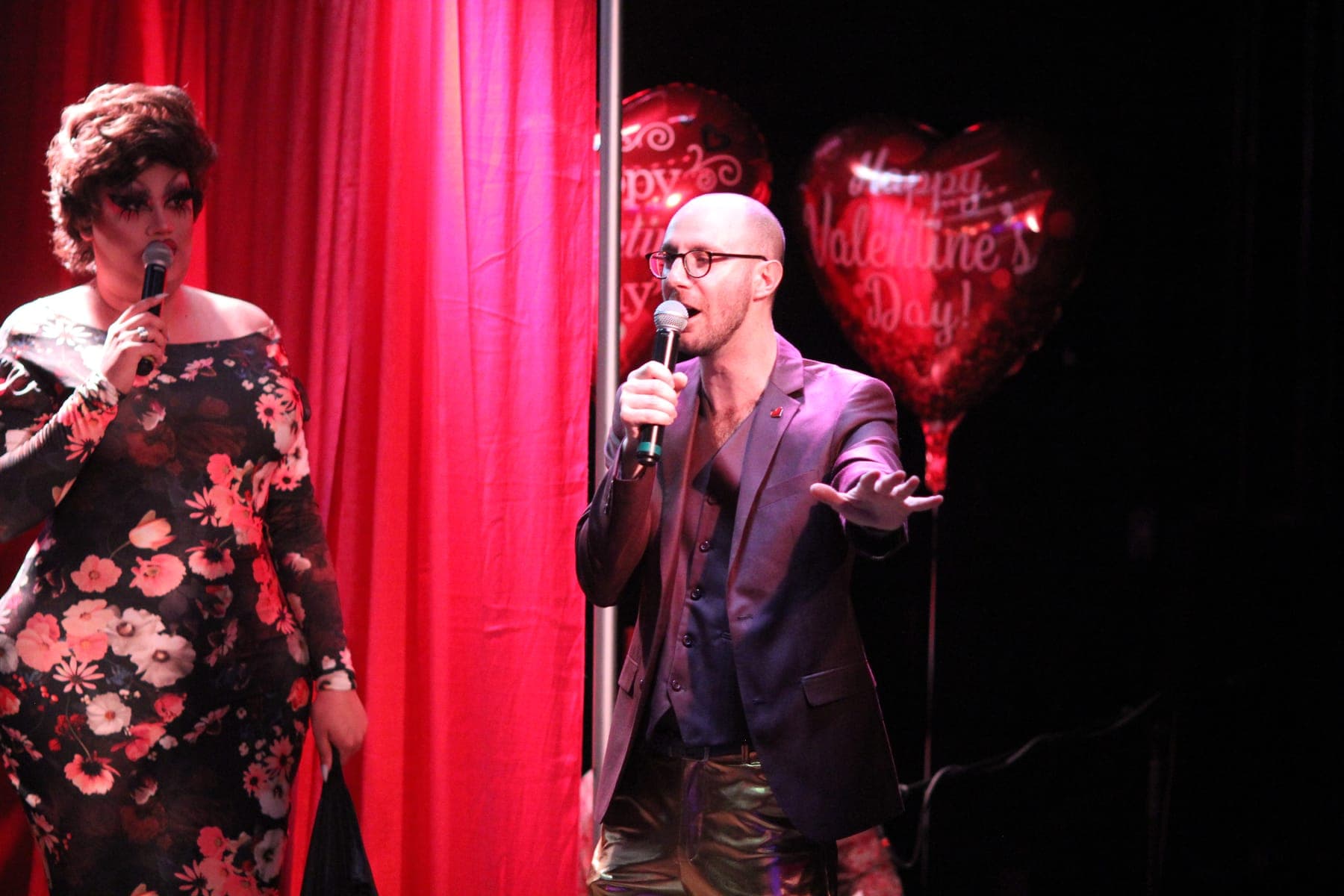 Max hosting in front of red curtains and Valentine's Day balloons