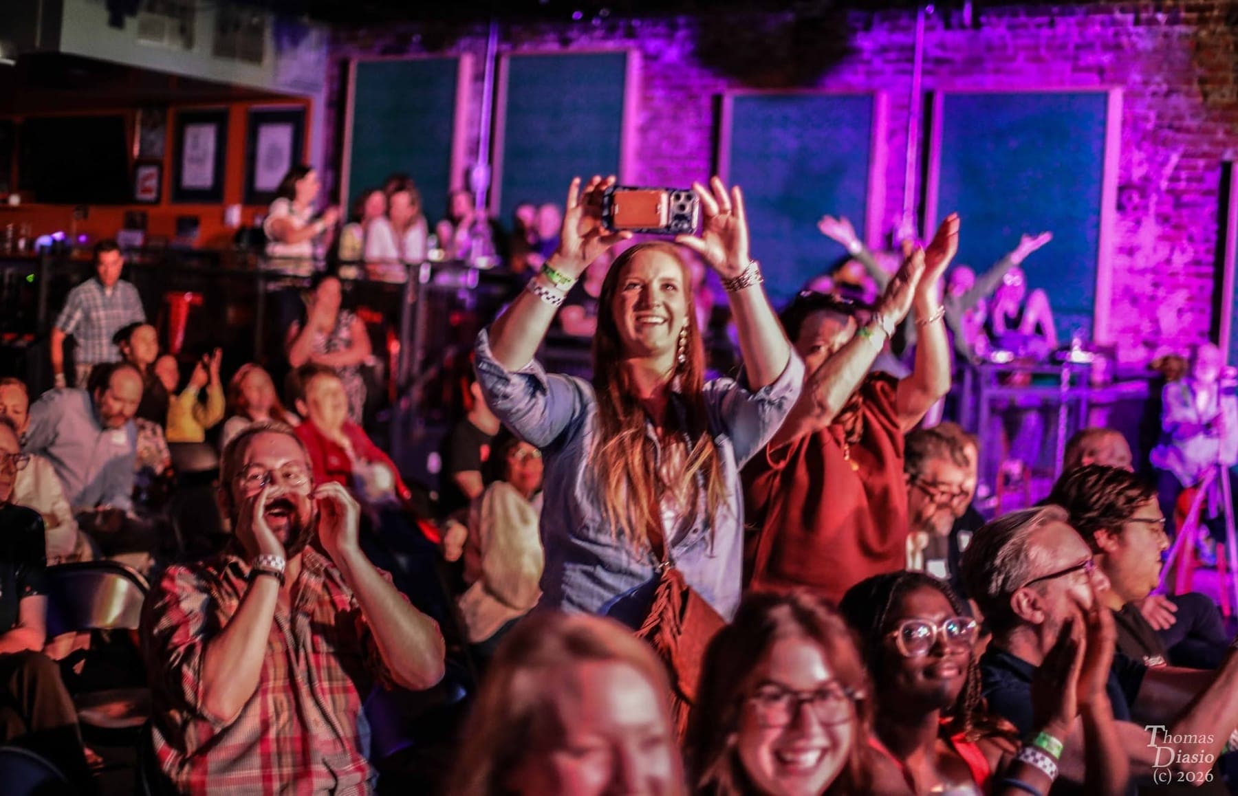 Audience members cheering, laughing, and filming the stage