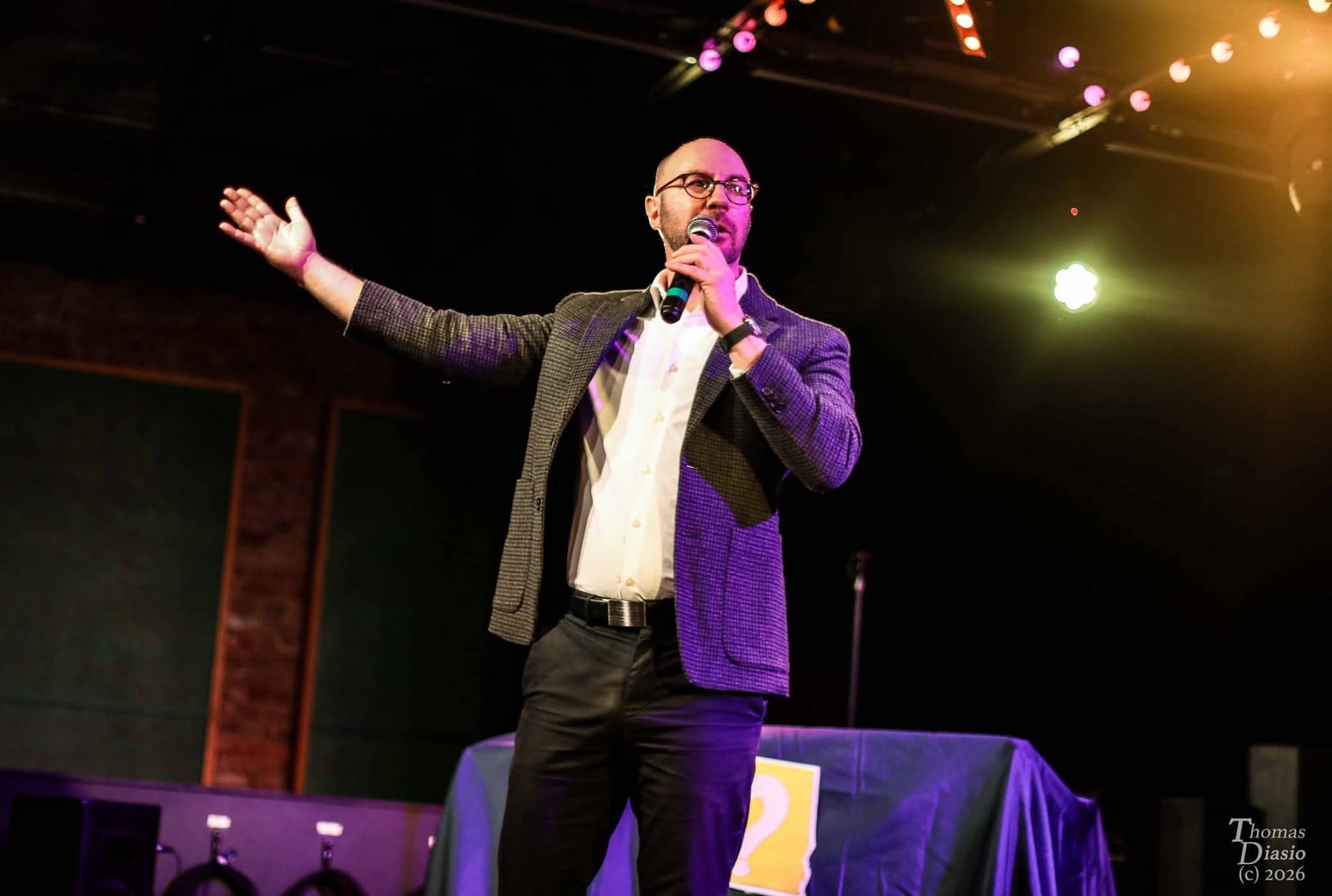 Max on stage with a microphone, arm outstretched toward the audience